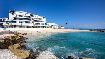 A beachfront hotel with multiple floors, a sandy beach, and a rocky shoreline.