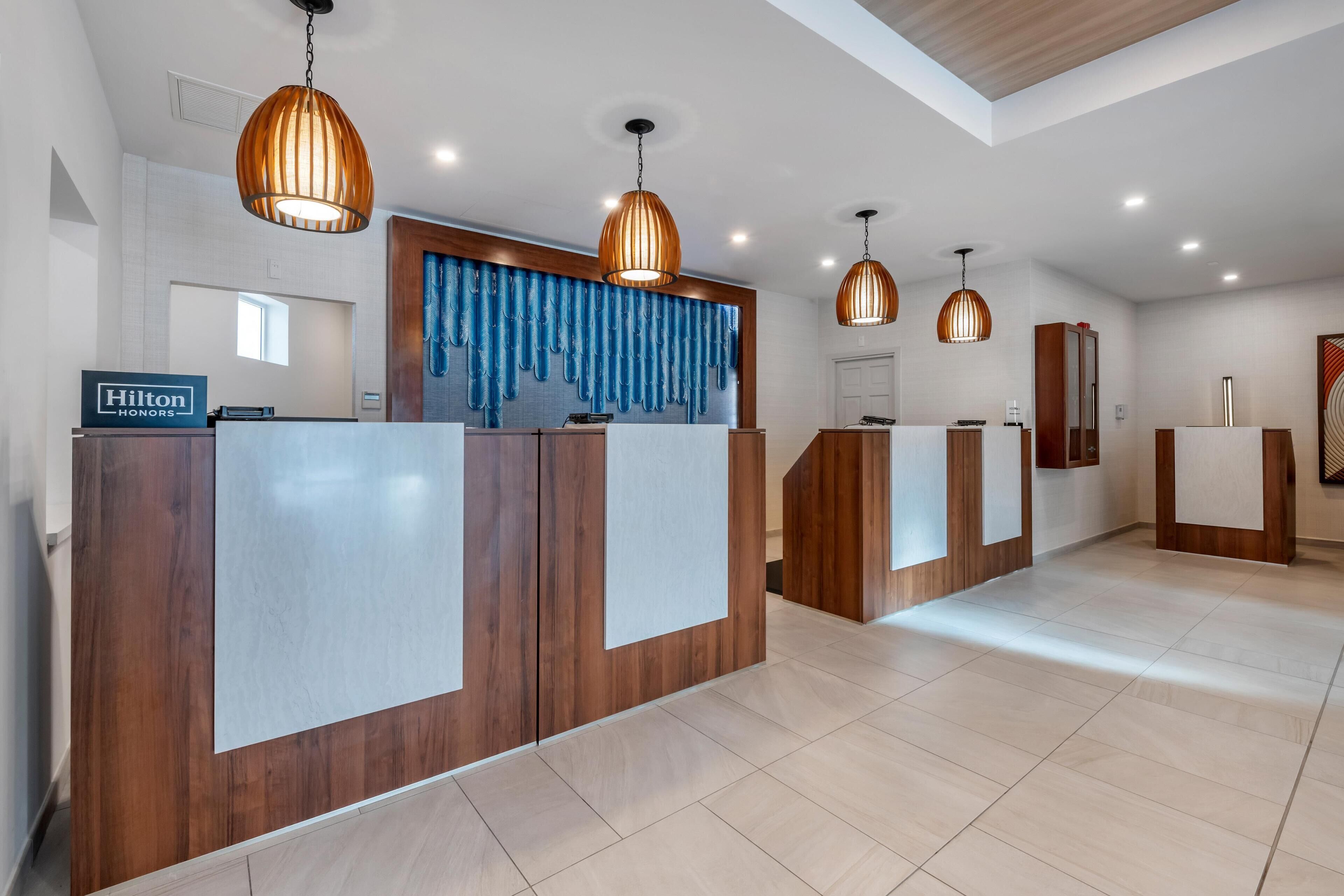 A hotel reception area with wooden reception desks, a blue decorative wall, and pendant lighting.