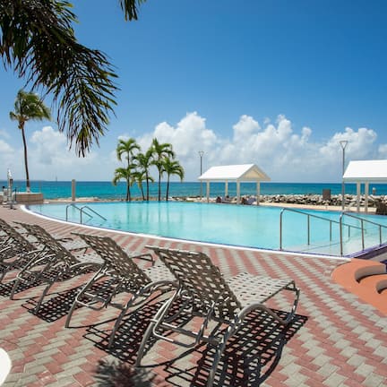 A poolside area with lounge chairs, a small pavilion, and a view of the ocean.