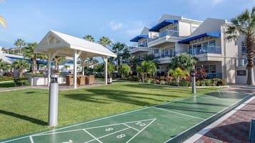 A shuffleboard court, a covered seating area, and a building with balconies and a blue awning.