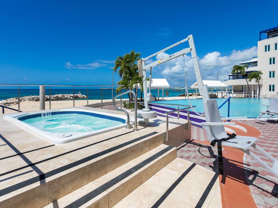 A rooftop pool area with a hot tub, lounge chairs, and a view of the ocean.