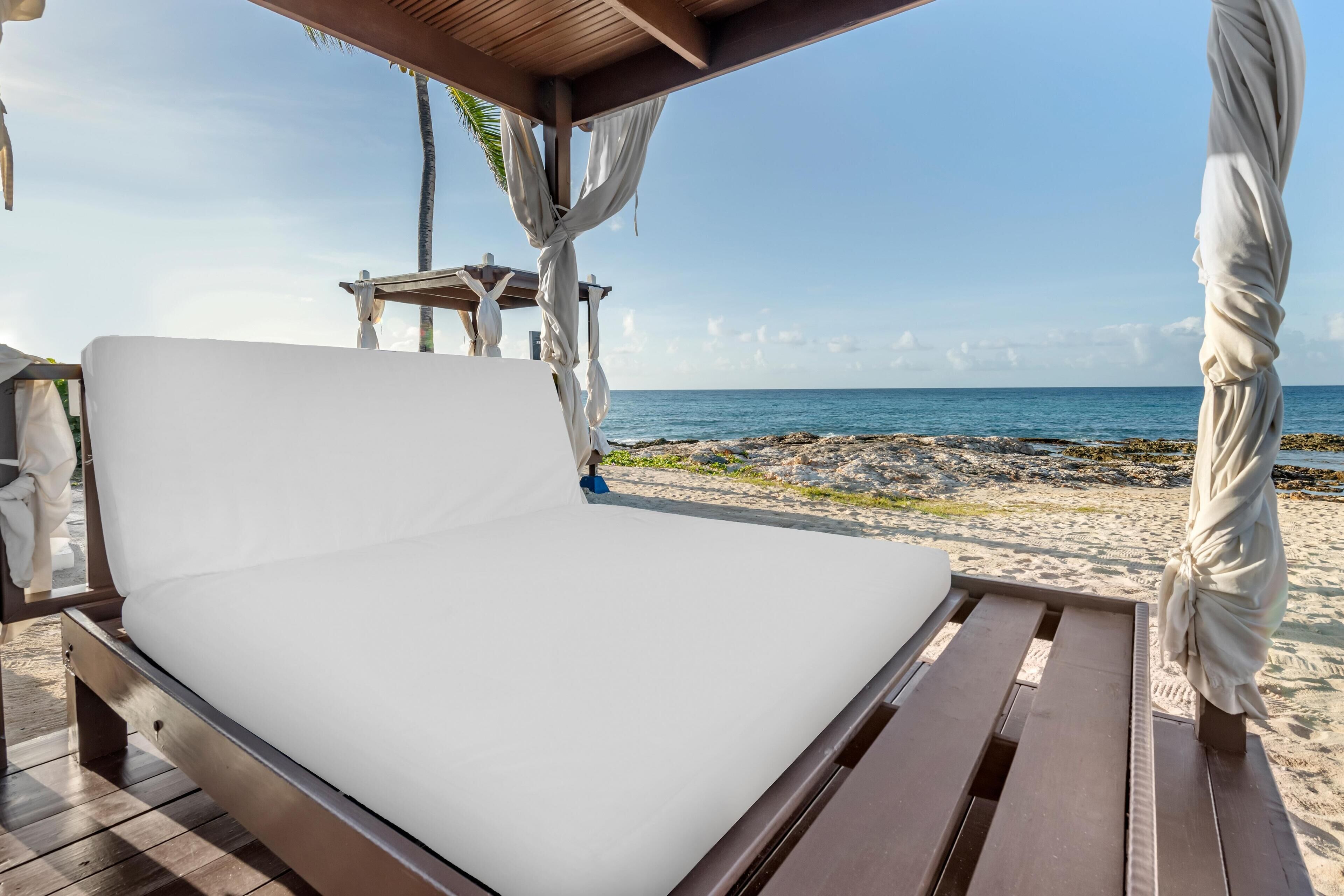 A bed with a white mattress, wooden frame, and a view of the ocean.