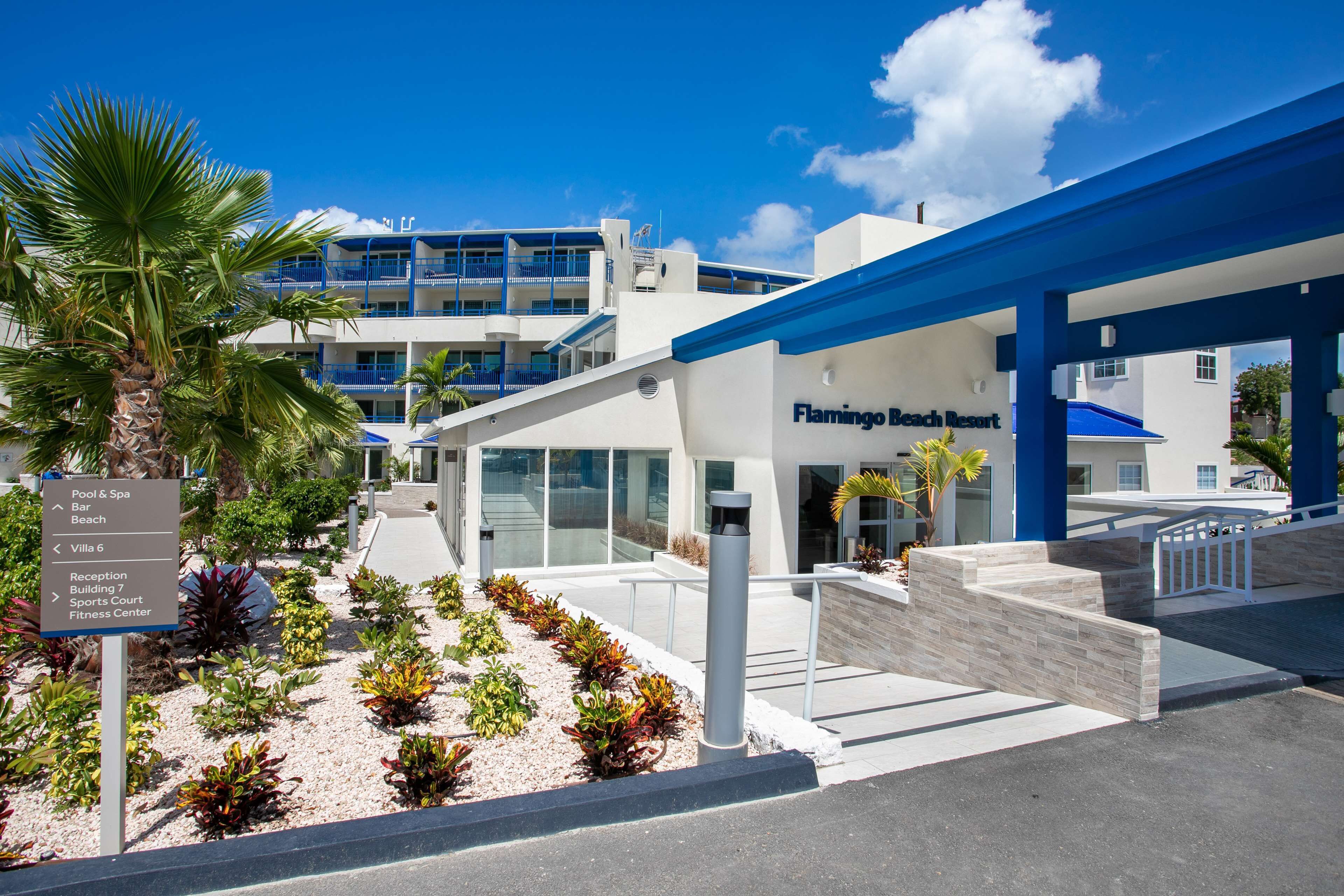 Ein moderner Hotelzugang mit Schild, das Einrichtungen wie Pool, Spa, Bar, Strand und Fitnesscenter anzeigt.