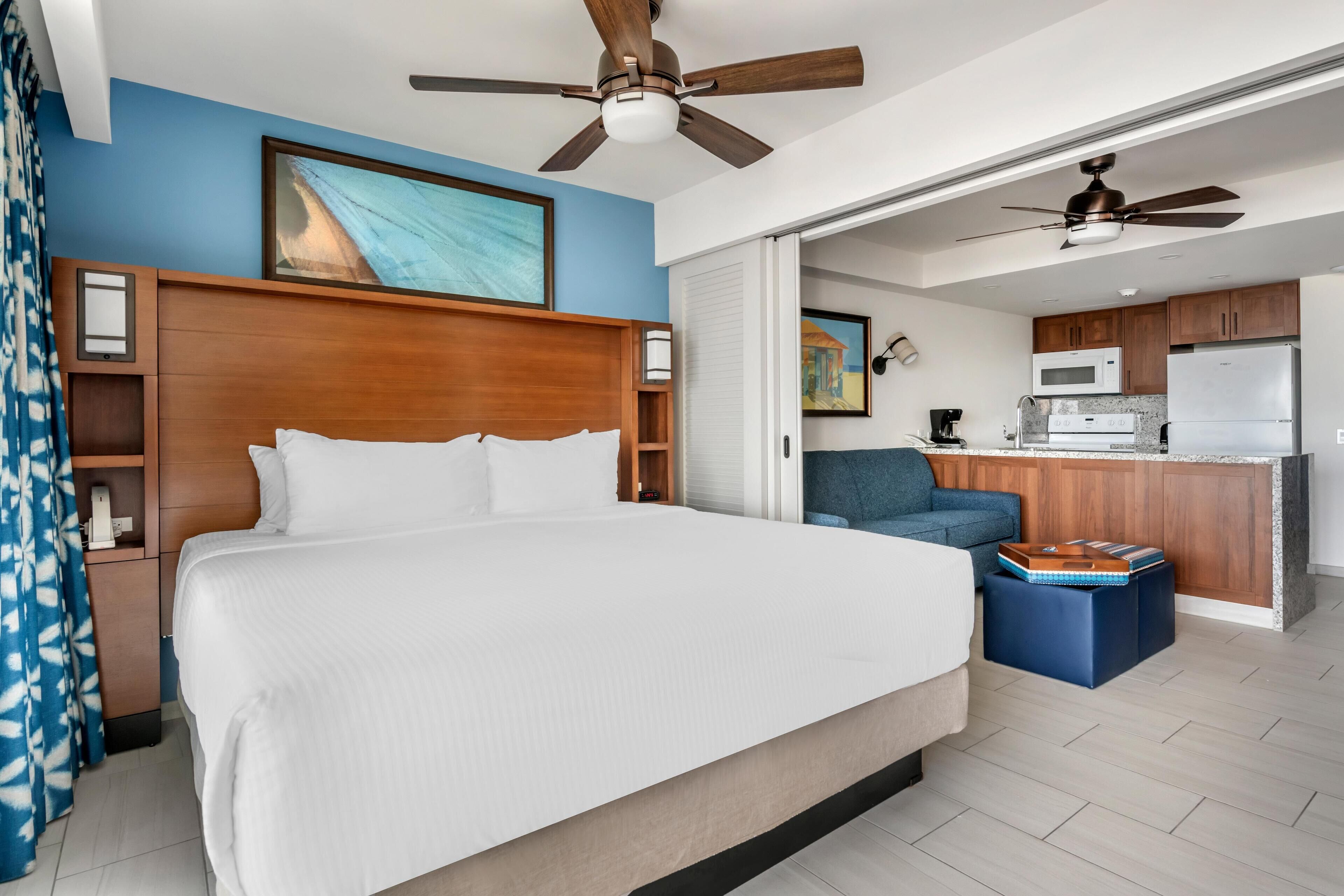 Een hotelkamer met een groot bed, een plafondventilator, een kitchenette en uitzicht buiten.