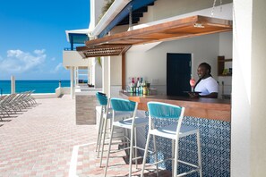 A bar area with a view of the ocean, bar stools, and a counter.