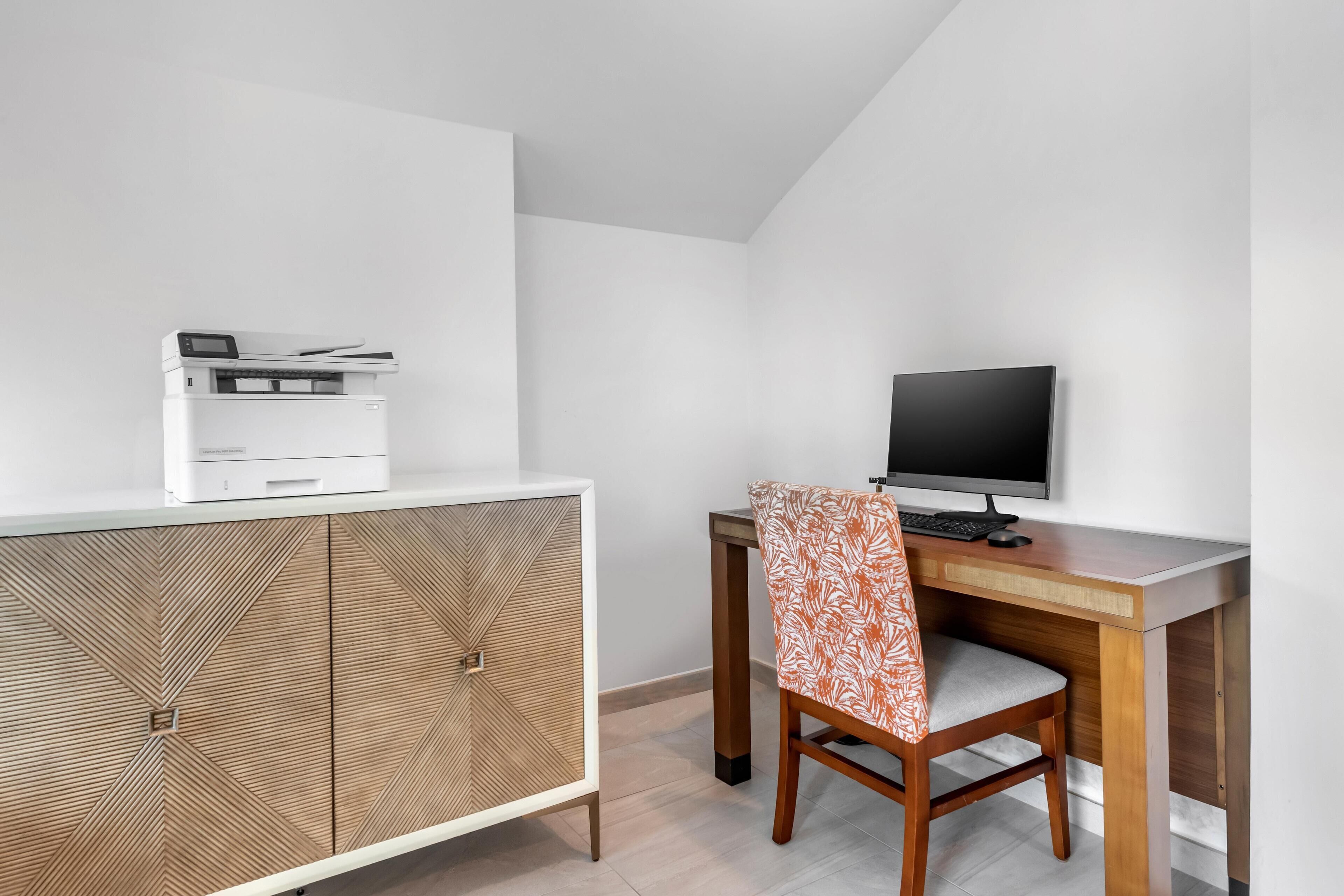 A modern office space with a white cabinet, a wooden desk, a computer monitor, and a printer.