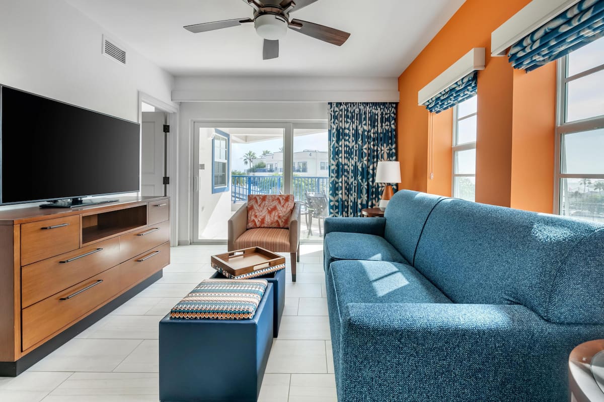 A modern living room with a large flat-screen TV, a blue sofa, a wooden cabinet, and a ceiling fan.