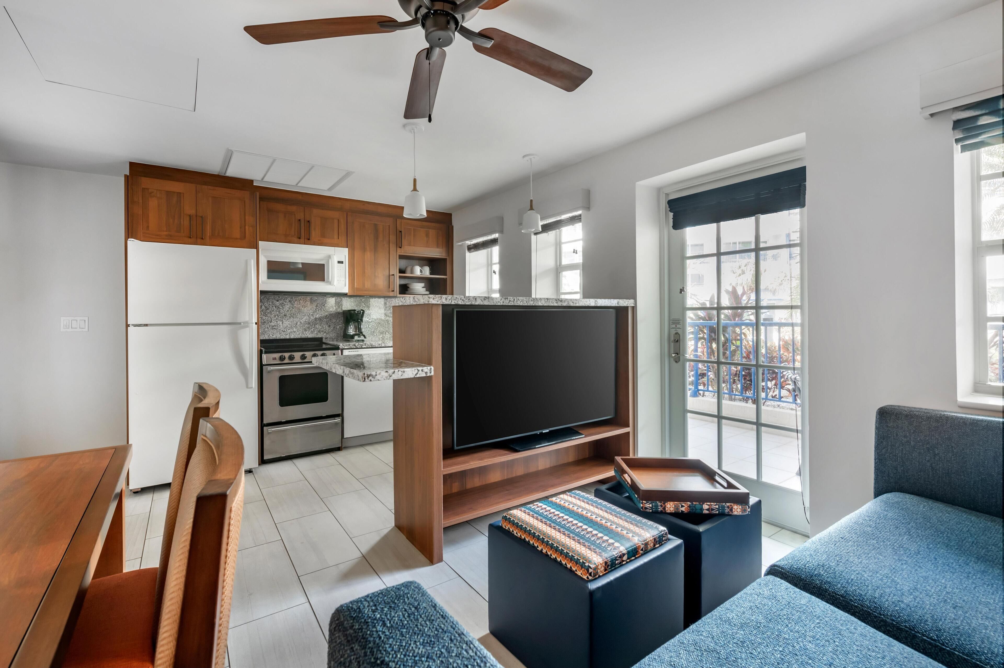 A modern kitchen with wooden cabinets, a built-in oven, and a large flat-screen TV.