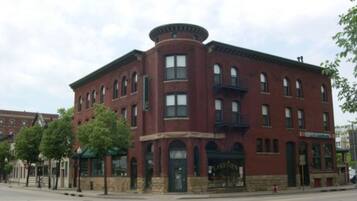 A red brick building with a corner entrance, large windows, and a balcony on the second floor.