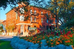 A brick building with a green awning, surrounded by colorful flowers and trees. - Hotel Ruby Marie (Madison)