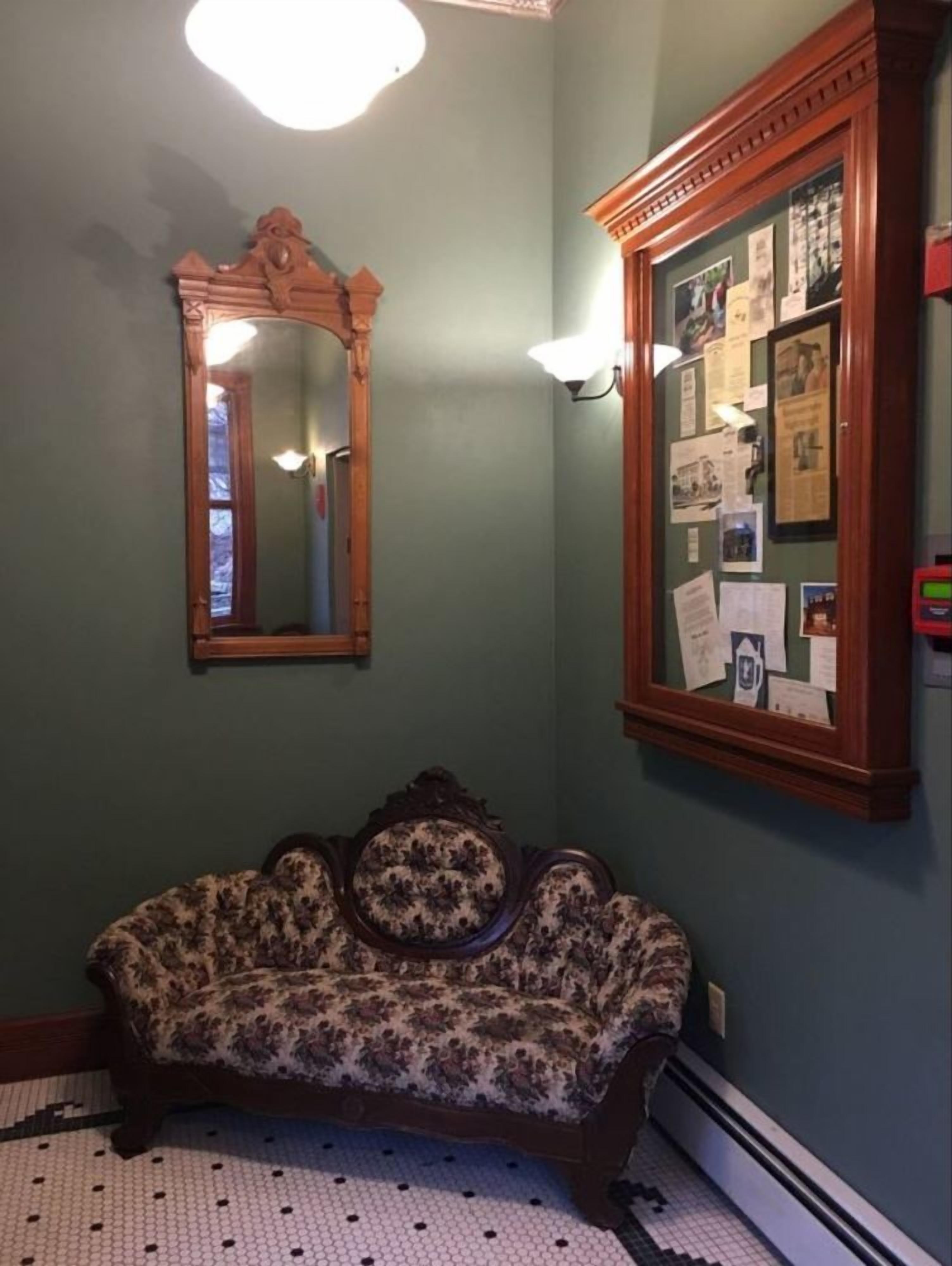 A room with a floral-patterned sofa, a mirror, and a bulletin board with papers.