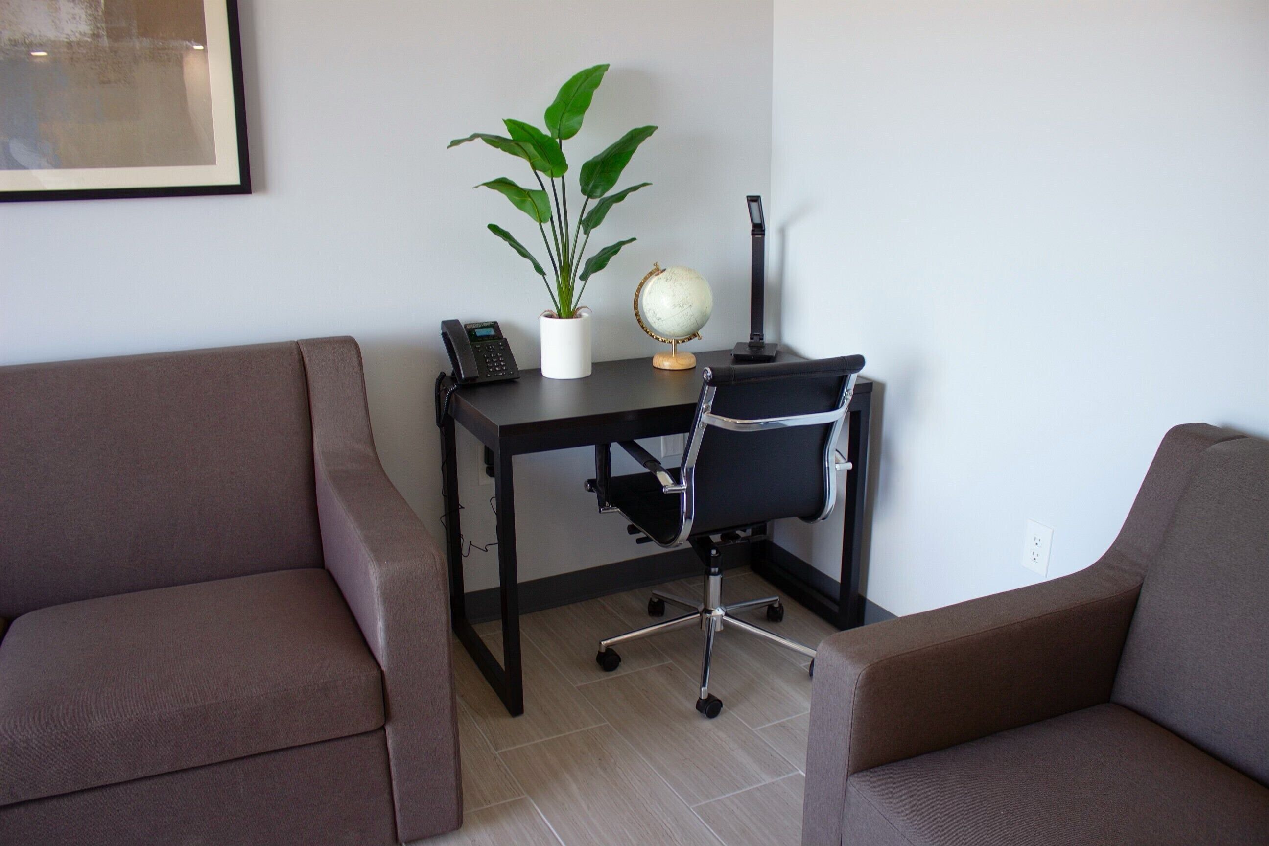 Una habitación con dos sofás marrones, un escritorio negro con un globo terráqueo y una planta, y un teléfono.