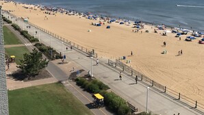 A beach with a paved walkway, umbrellas, and people. - Sun and Sand Resort Oceanfront Suites  (Virginia Beach)