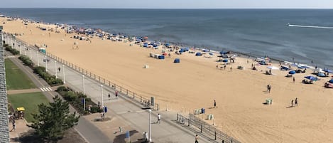 A beach with a paved walkway, umbrellas, and people.