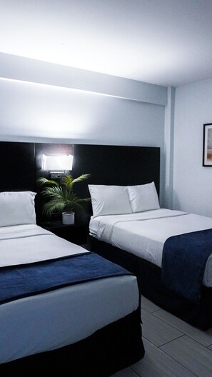 A hotel room with two single beds, a nightstand with a lamp, and a potted plant. - Sun and Sand Resort Oceanfront Suites  (Virginia Beach)