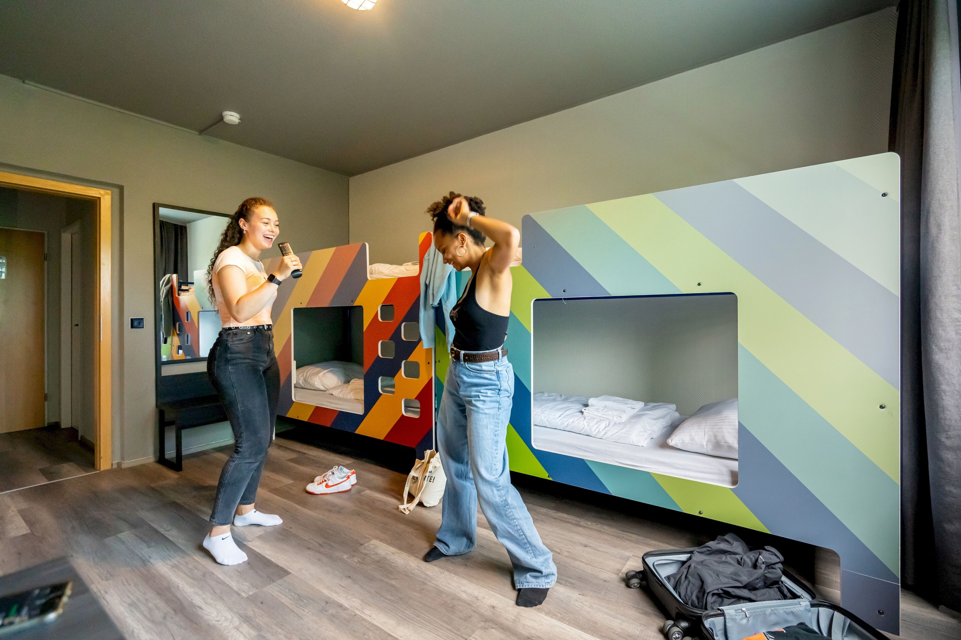 Een moderne hotelkamer met stapelbedden, een koffer en een spiegel.