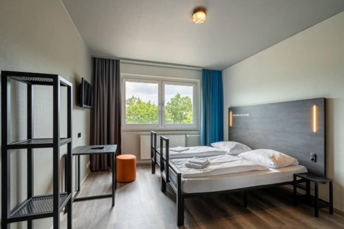 A modern hotel room with a bed, a desk, a chair, and a TV.