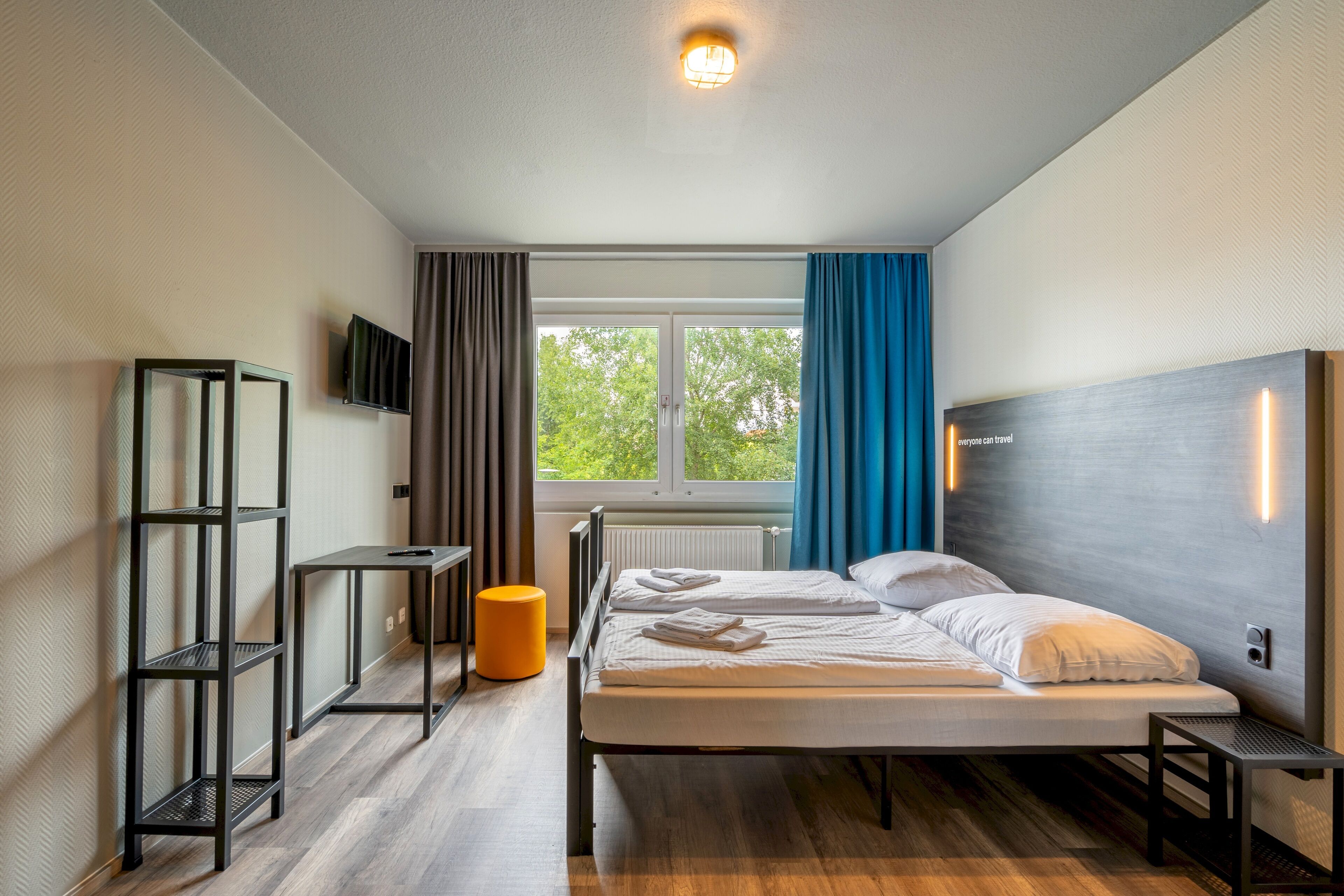 Una habitación de hotel moderna con una cama, un televisor en la pared y una ventana con cortinas.