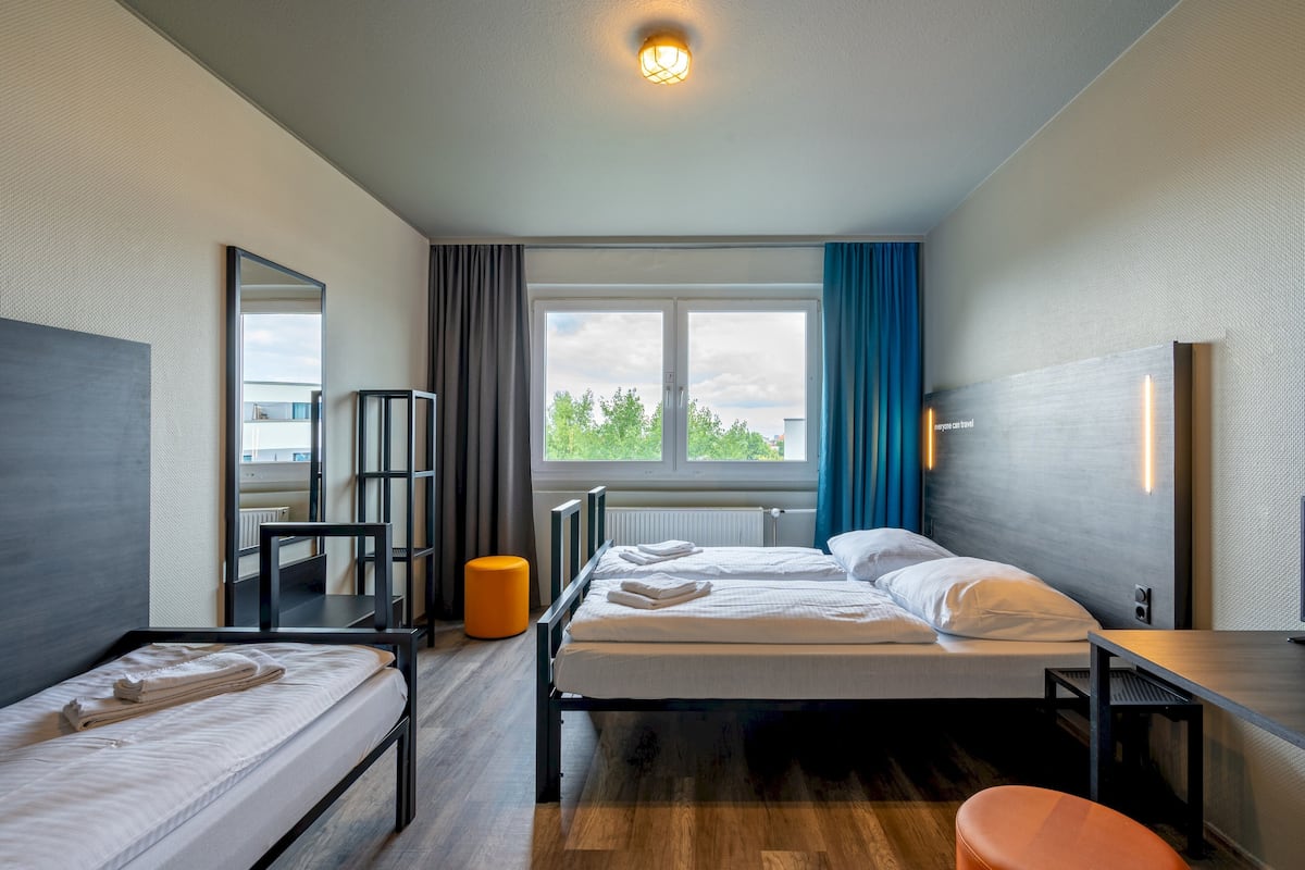 A modern hotel room with two beds, a desk, a chair, a mirror, and a window with curtains.
