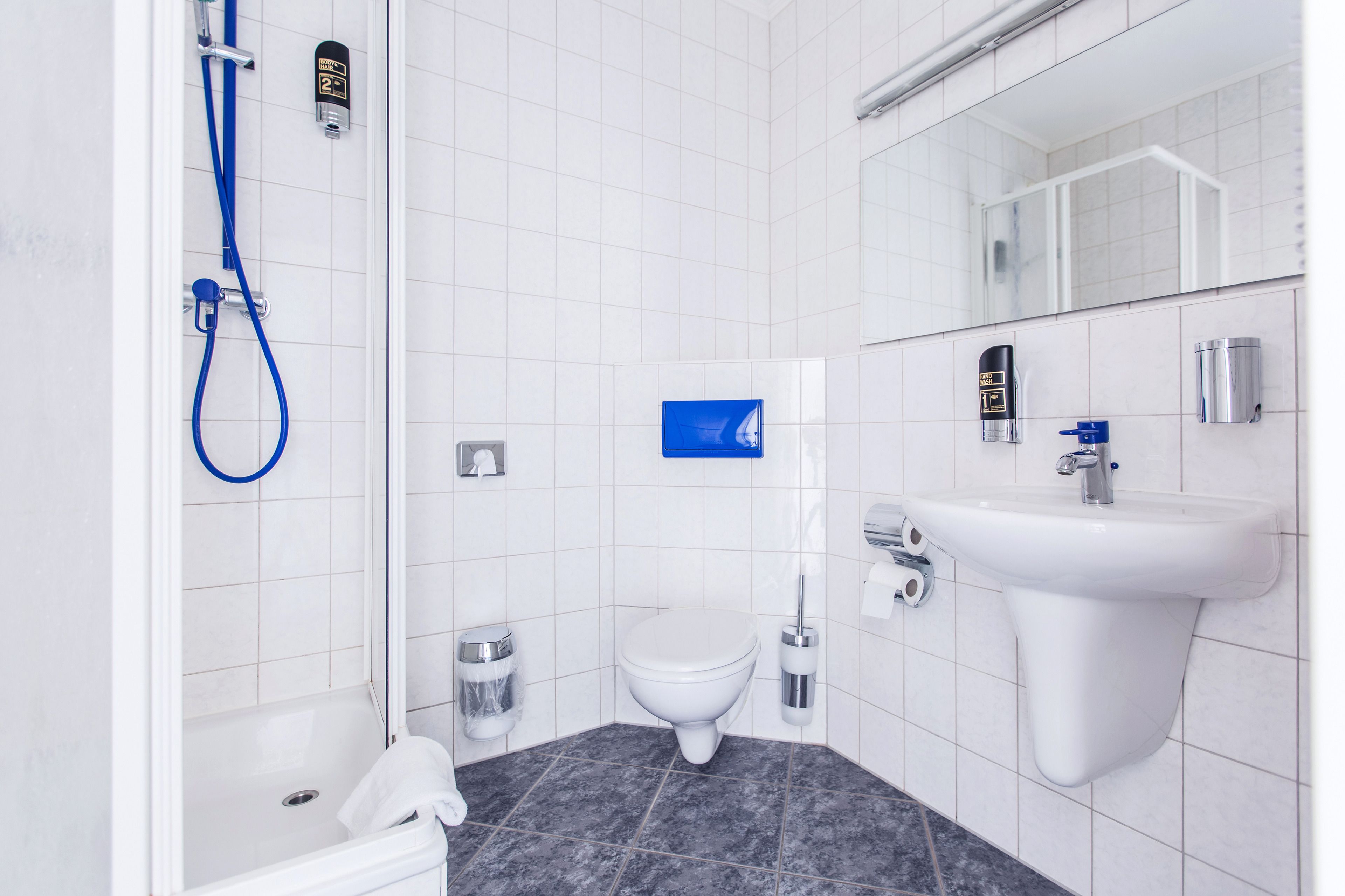 Een moderne badkamer met witte tegels, een douche, toilet, wastafel en spiegel.