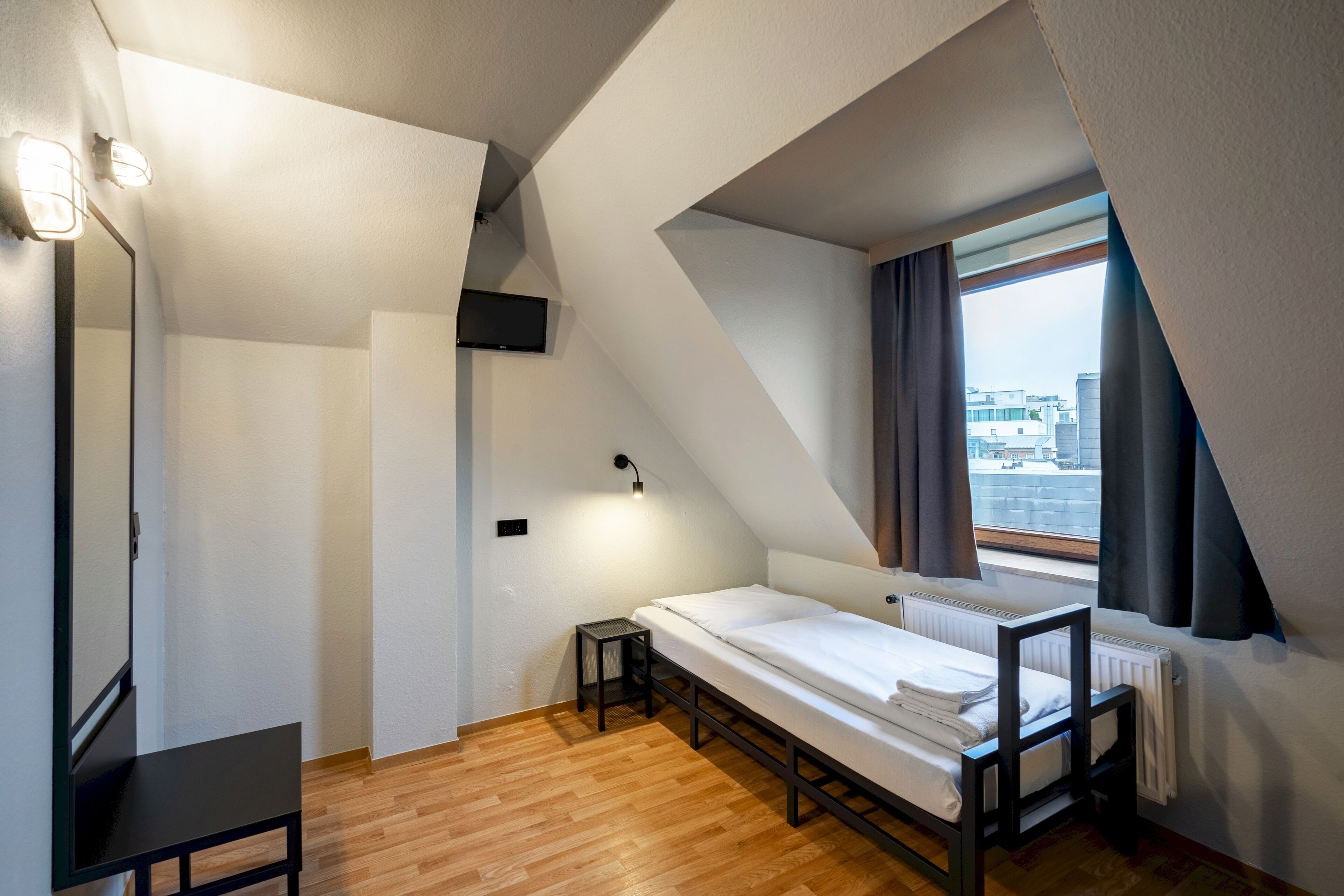 Een compacte, moderne slaapkamer met een bed in open loftstijl, een klein tafeltje en een raam met gordijnen.