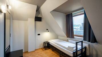 Ett litet, modernt sovrum med en säng i loftstil, ett litet bord och ett fönster med gardiner.