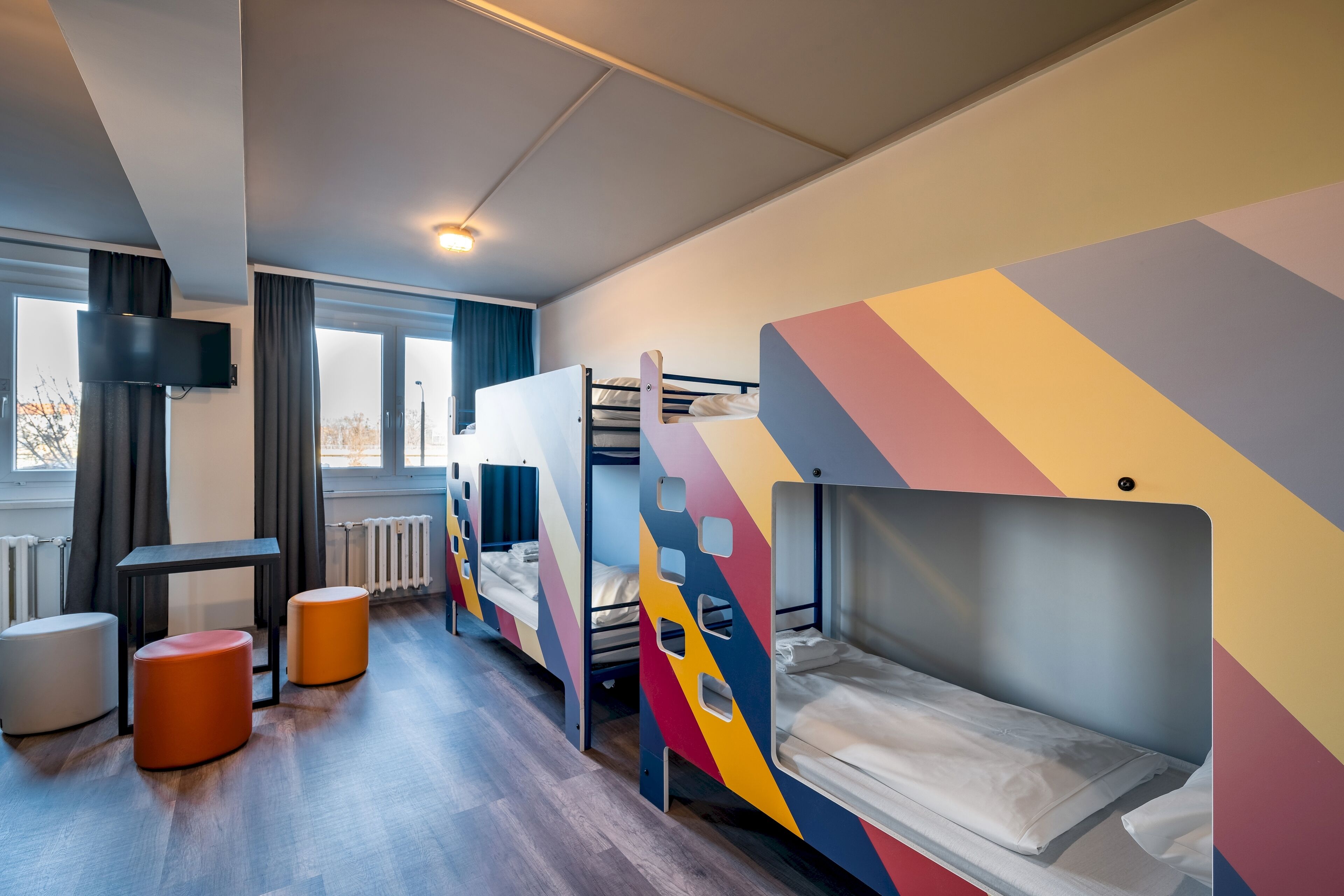Habitación tipo dormitorio con literas, un escritorio y dos otomanes.