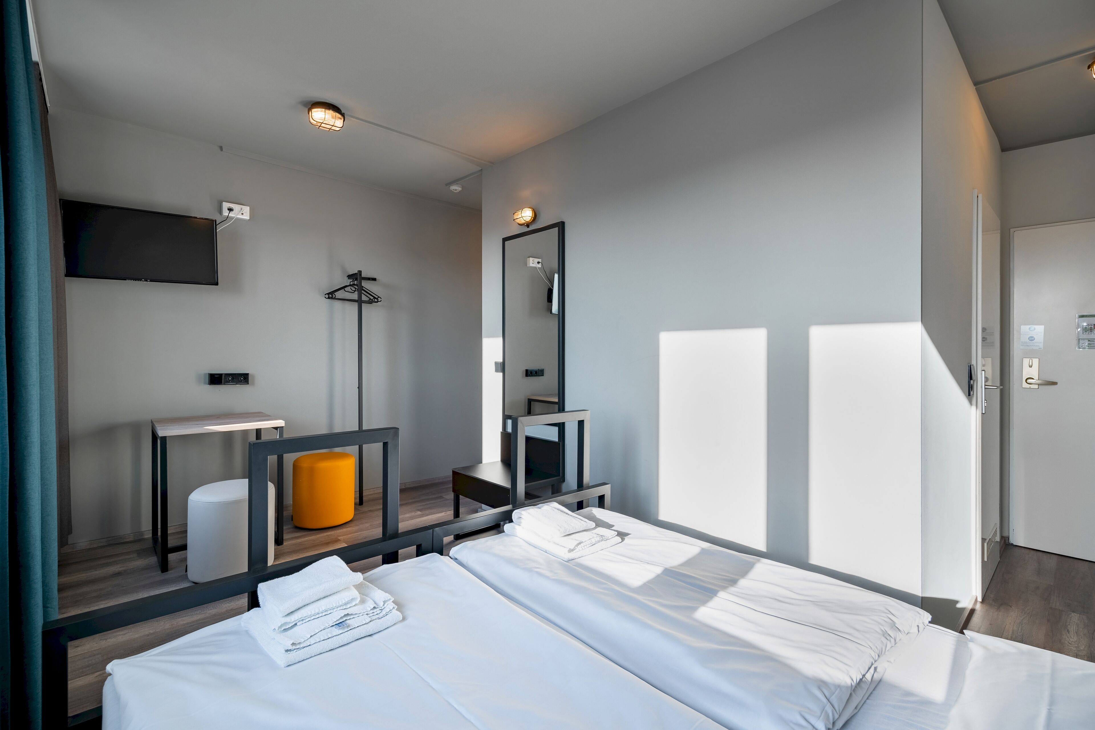 A modern hotel room with a bed, a desk, a chair, a mirror, and a TV.