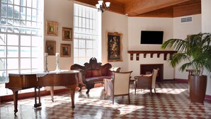 A spacious room with a checkered floor, a grand piano, a sofa, and a fireplace. - Beach Park Hotel (Miami Beach)