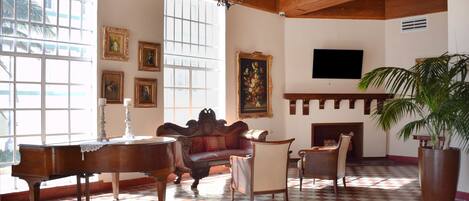A spacious room with a checkered floor, a grand piano, a sofa, and a fireplace.