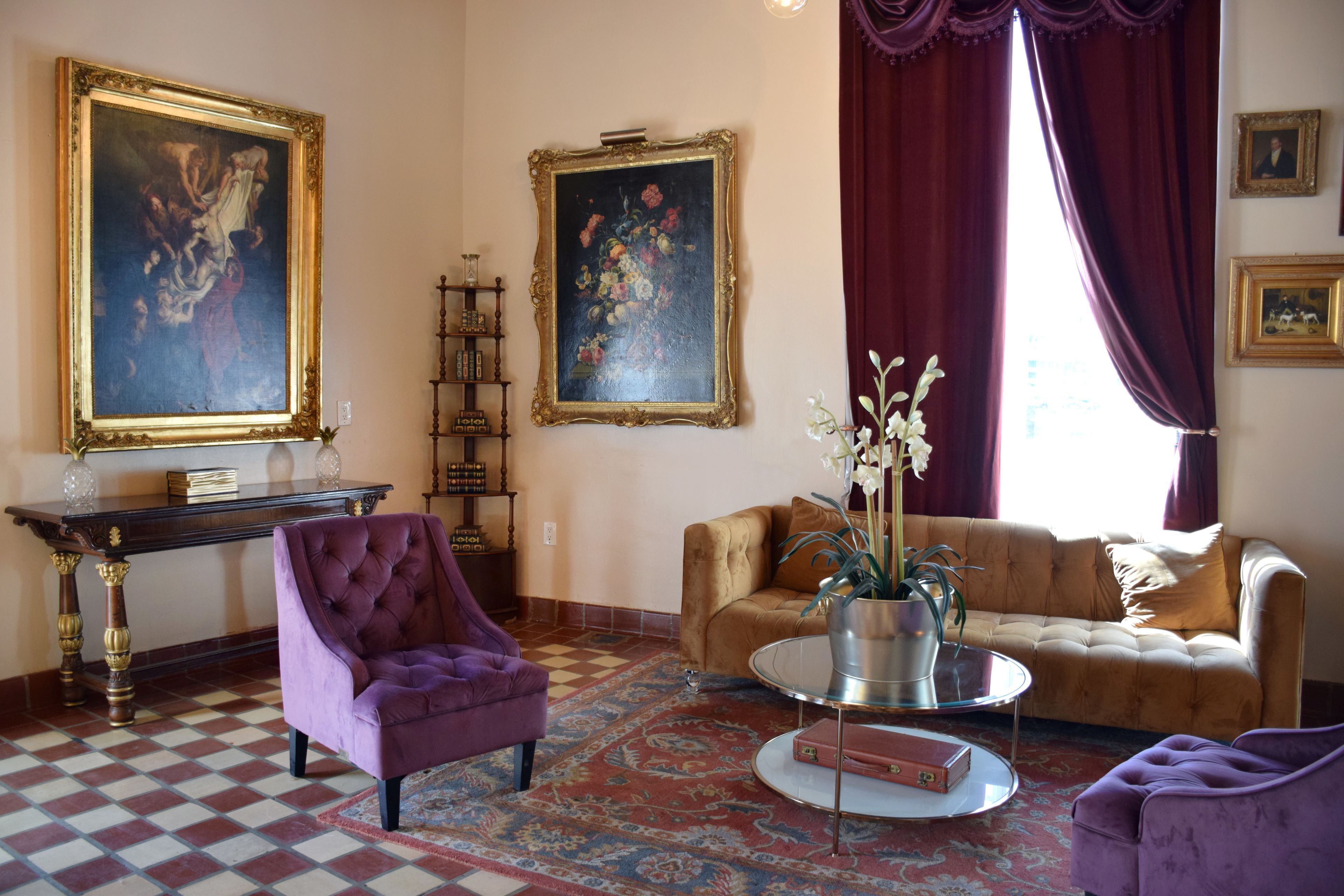 A living room with a checkered floor, a purple armchair, a sofa, a coffee table with a vase, and two paintings on the wall.