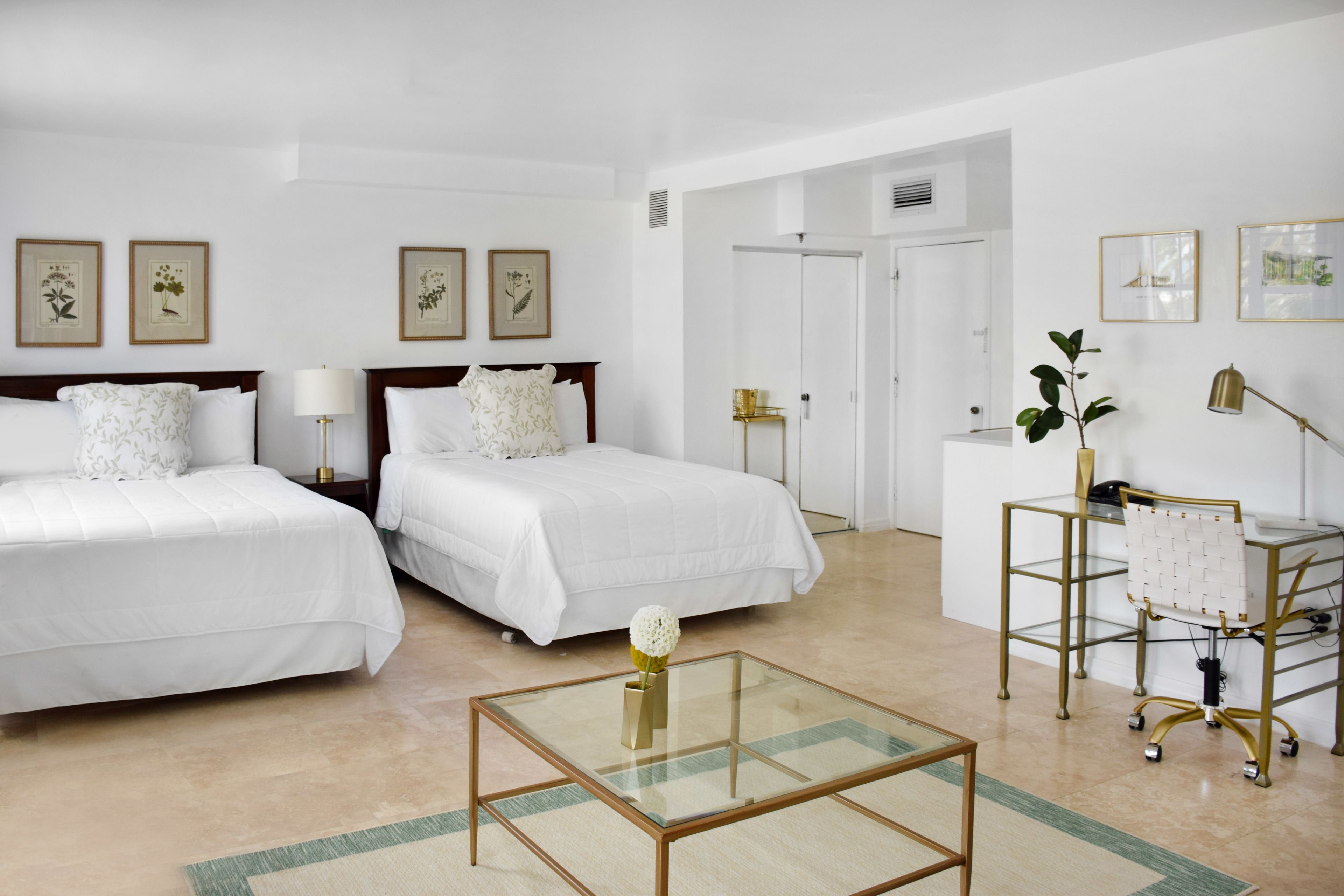 Een hotelkamer met twee bedden, een glazen salontafel, een bureau met stoel en lijstwerken met plantenmotieven op de muren.
