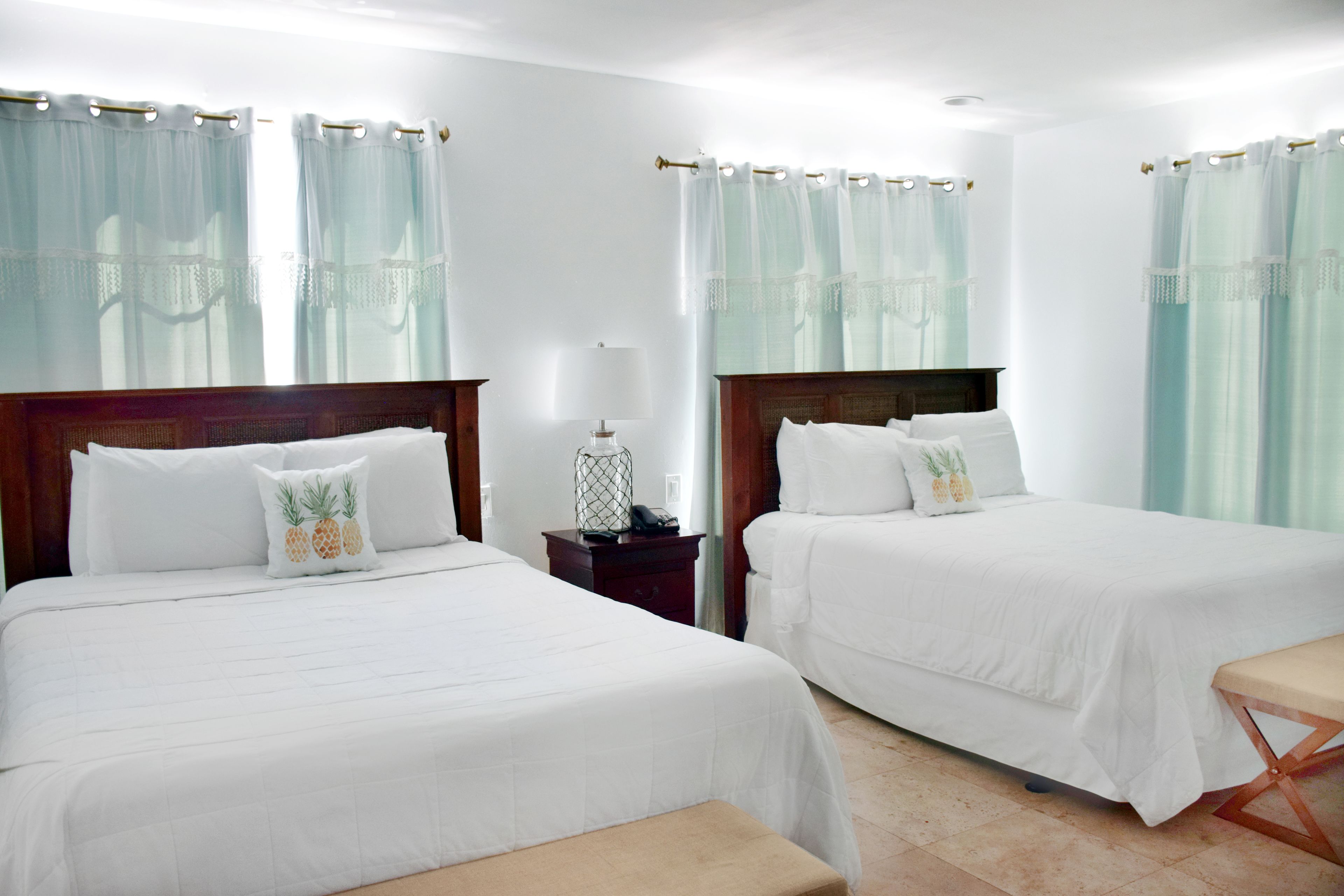 Une chambre d’hôtel avec deux lits, une table de chevet, une lampe et un banc.
