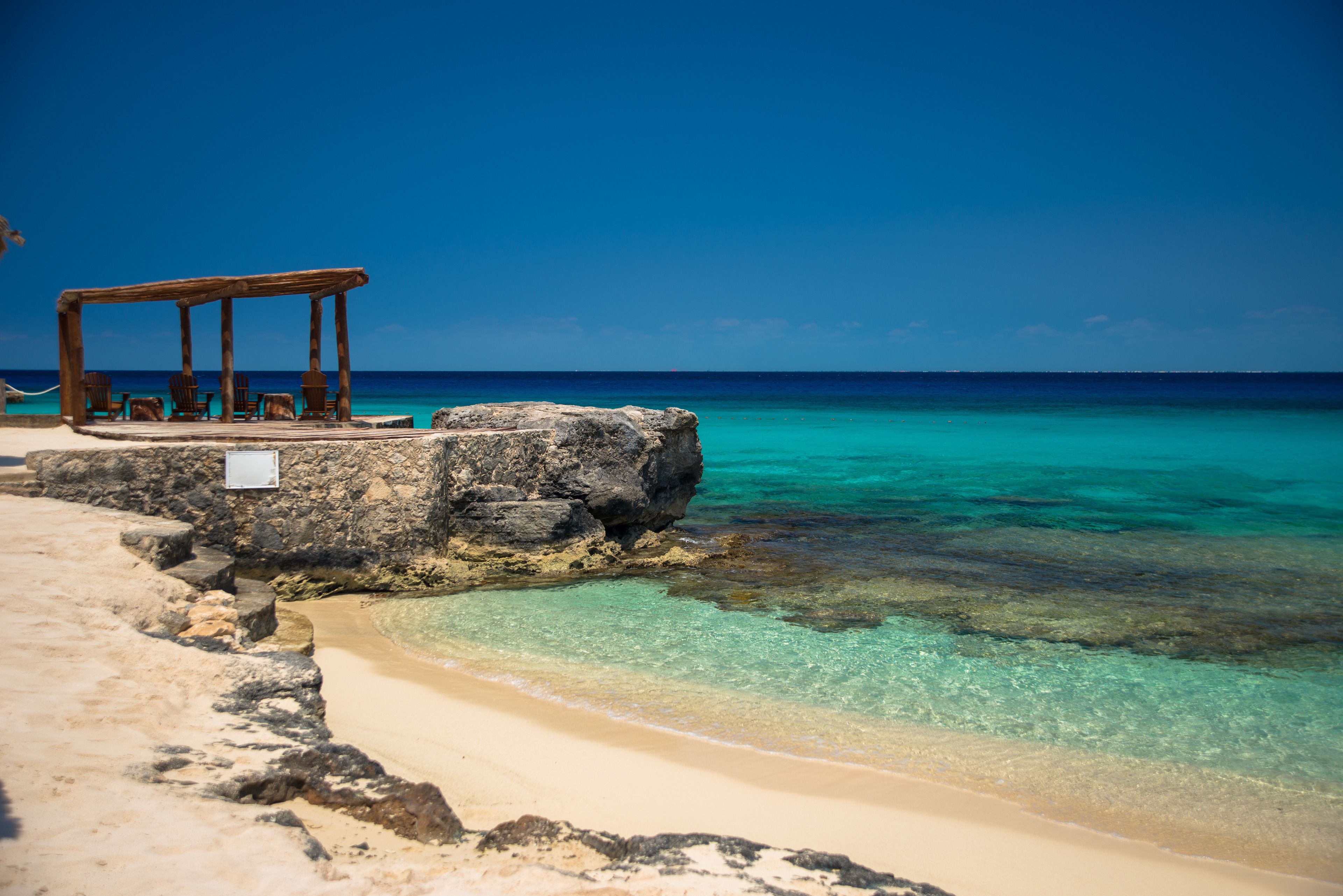 A beach with a wooden structure and a sign, clear turquoise water, and a sandy shore.