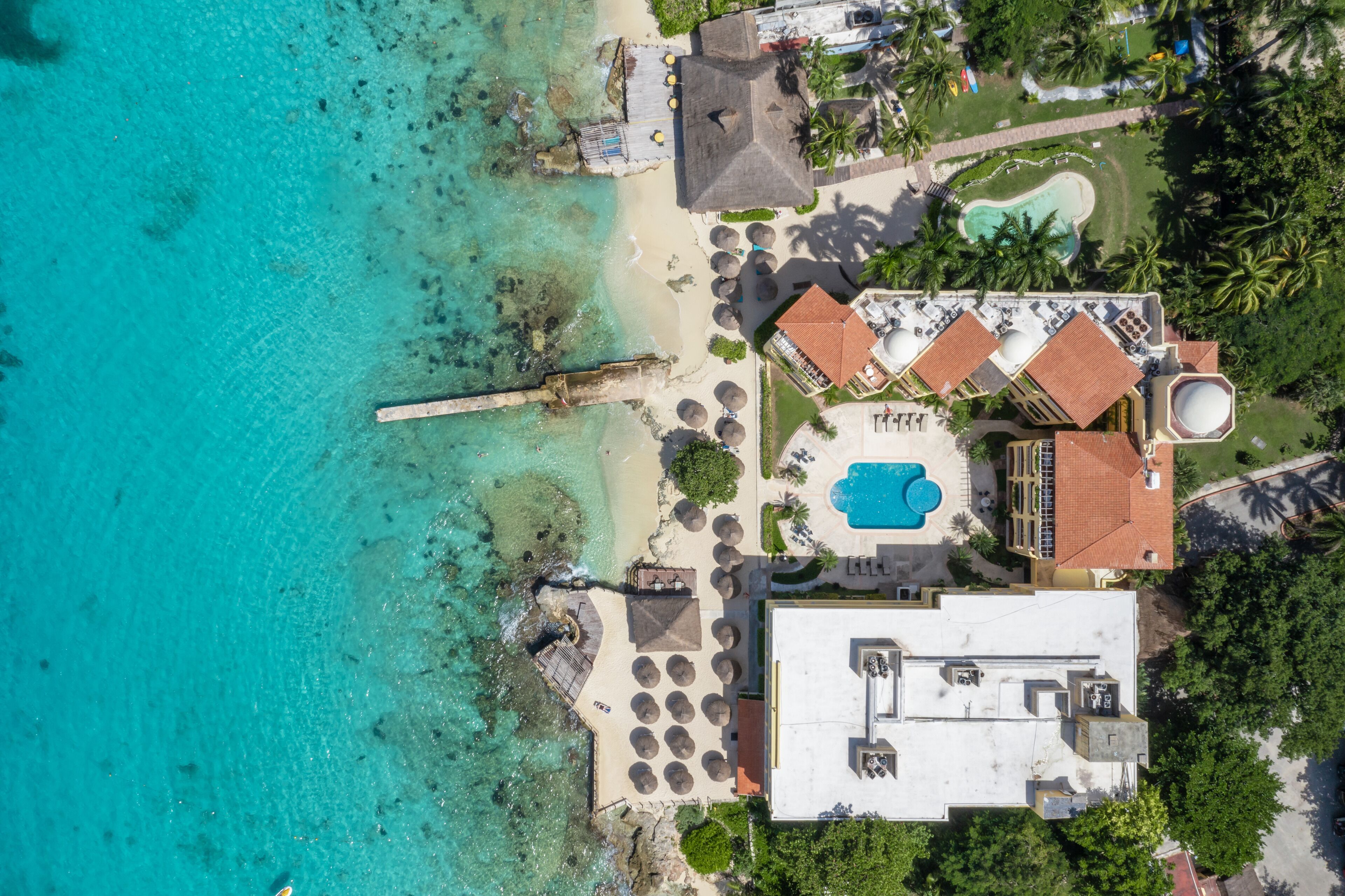 Luchtbeeld van een resort met een strand, een zwembad en een gebouw met een rood dak.