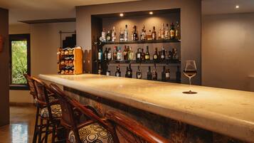 A bar area with a long counter, multiple chairs, and a variety of bottles on shelves.
