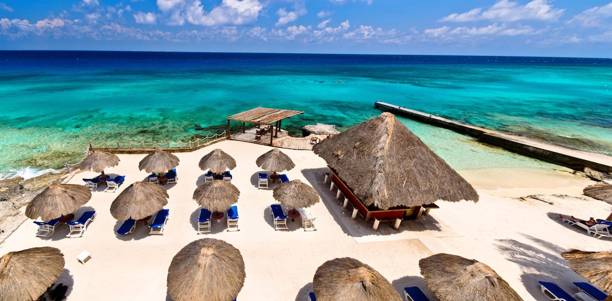 Straw umbrellas and lounge chairs on a white sandy beach over looking the beautiful blue waters of Cozumel.