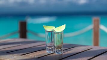 Two shot glasses with lime slices on a wooden table by a turquoise sea.