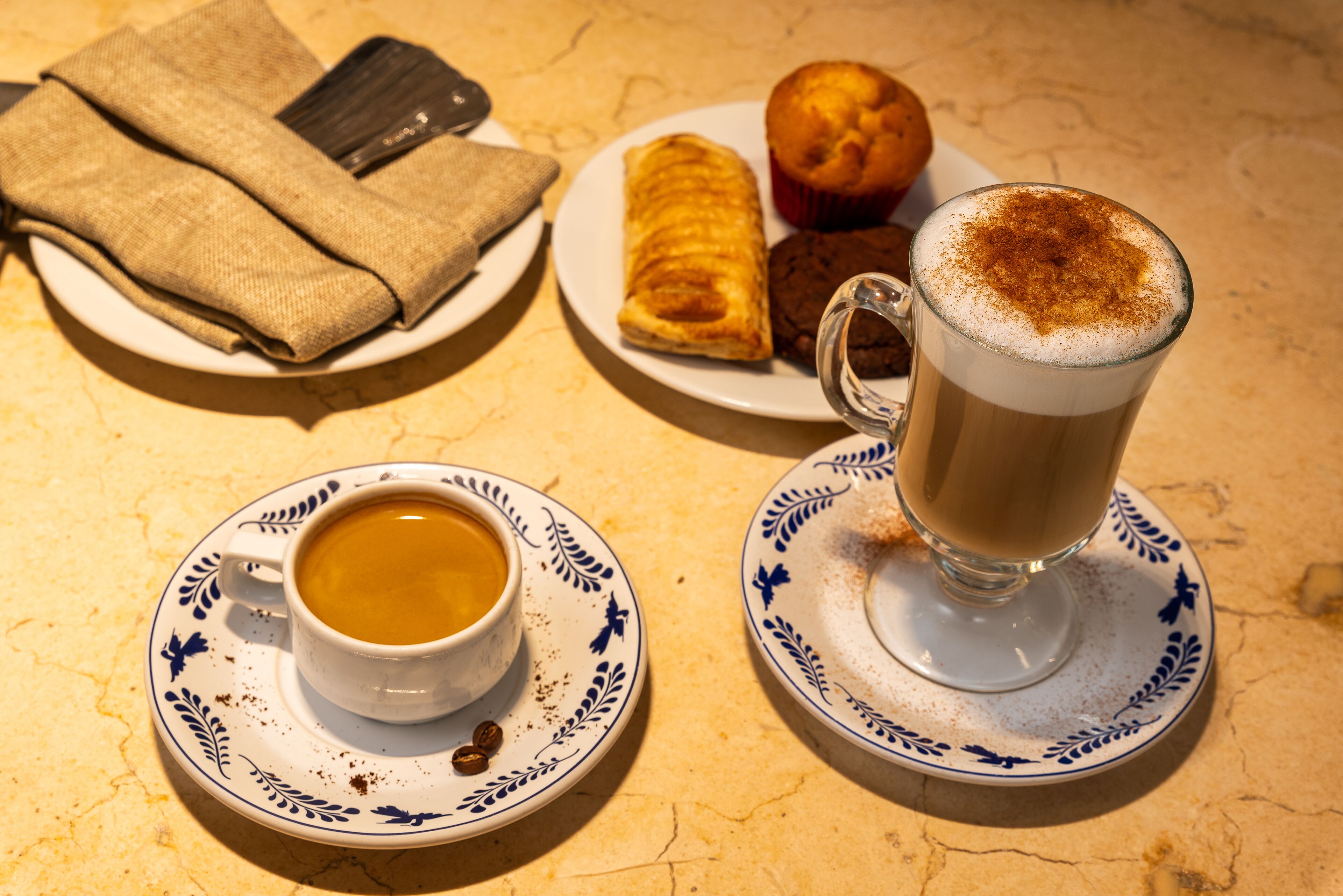 Une table avec une tasse de café, un muffin, une pâtisserie et un verre de café avec de la mousse.