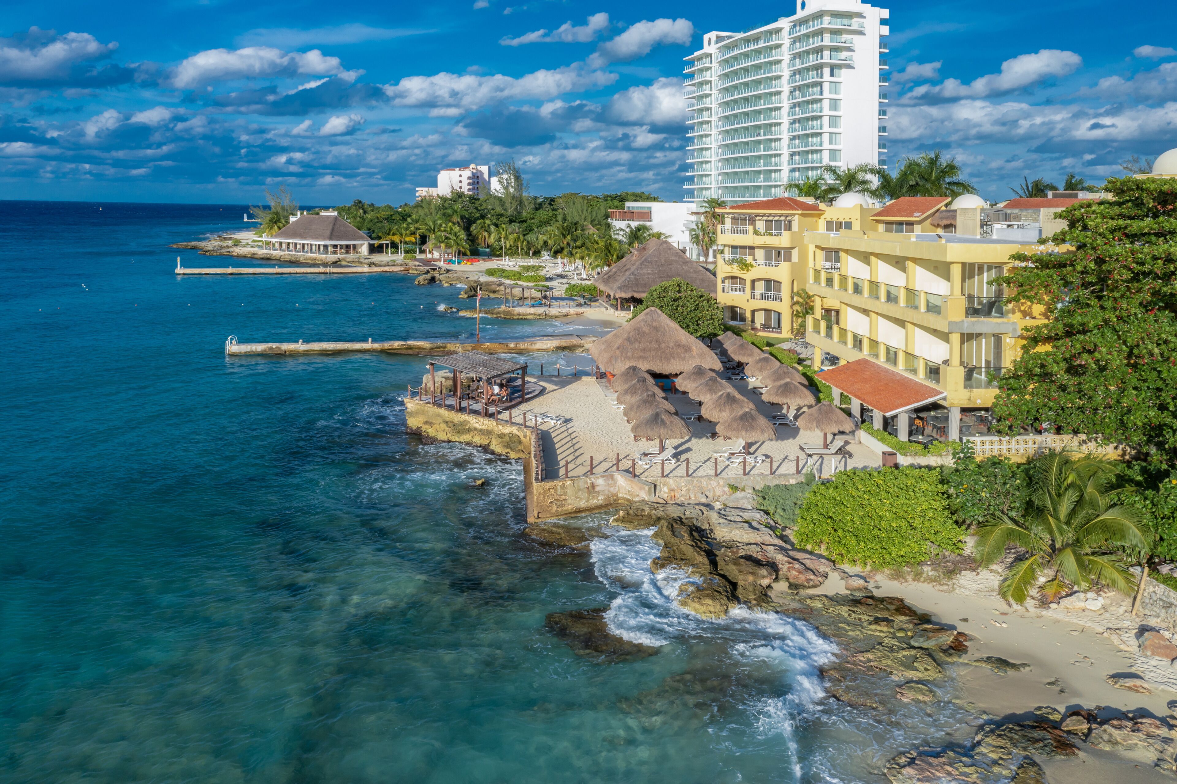 A coastal hotel with a beach view, a pier, and a tall building in the background.