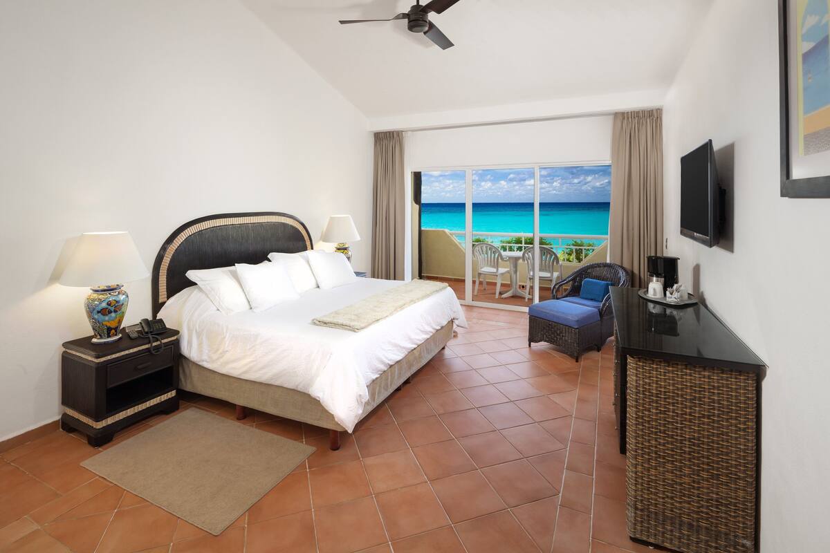 A hotel room with a bed, a desk, a television, and a balcony with a view of the ocean.
