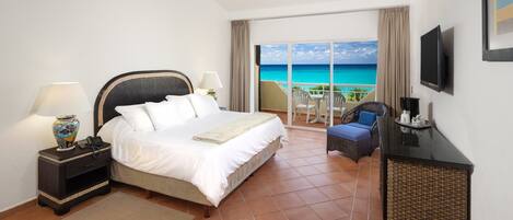 Quarto de hotel com cama, escrivaninha, televisão e varanda com vista para o oceano.