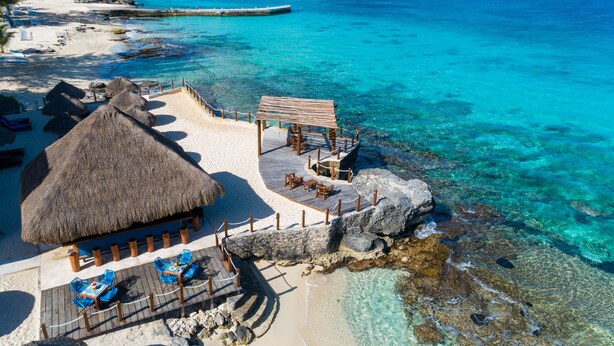 A beachside resort with a thatched-roof hut, a wooden deck with seating, and clear turquoise waters. - Hotel Playa Azul Cozumel (Cozumel)