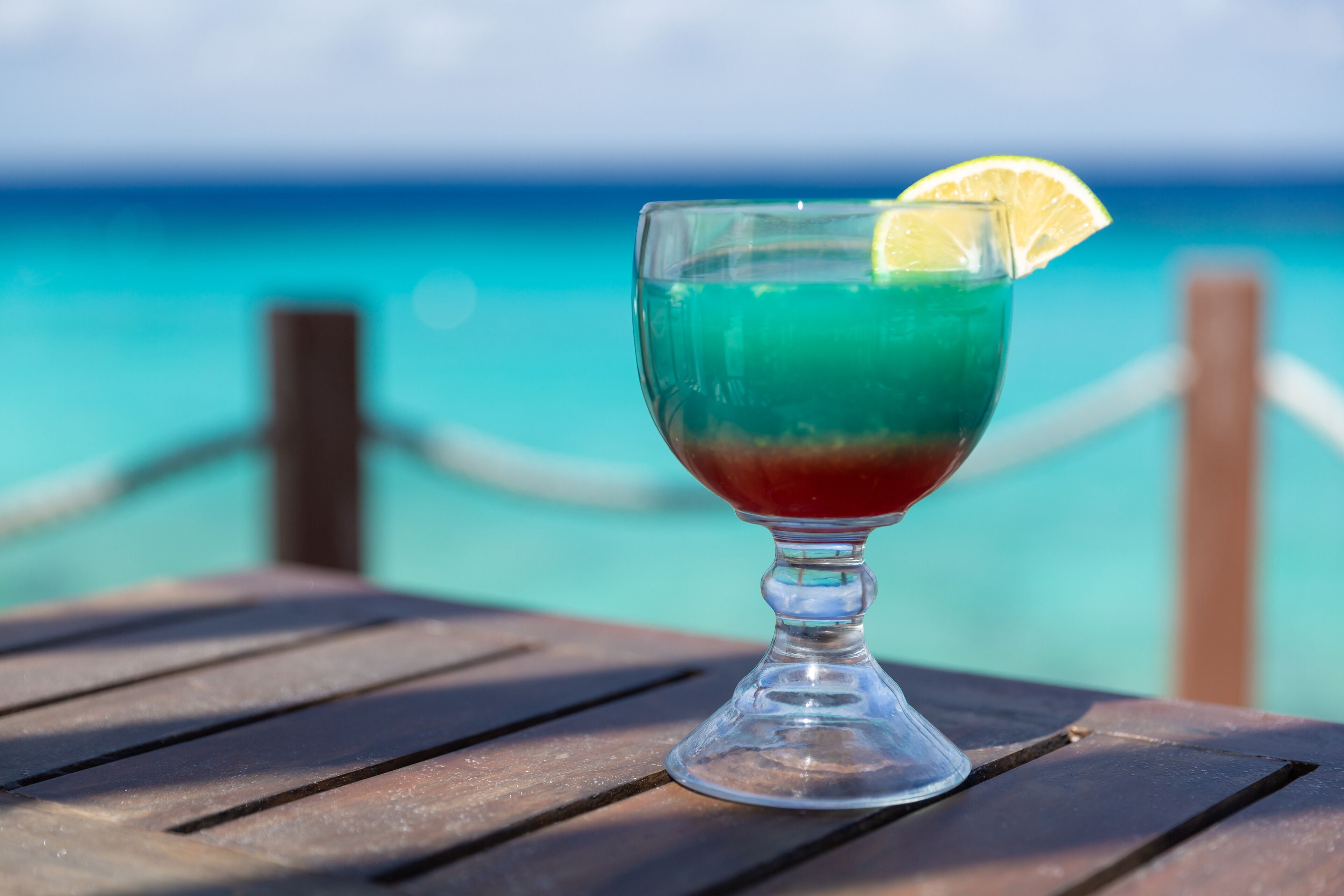 A cocktail glass with a slice of lemon on a wooden table by the ocean.