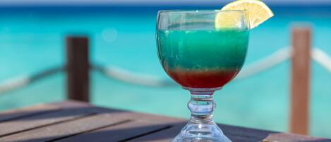 A cocktail glass with a slice of lemon on a wooden table by the ocean.