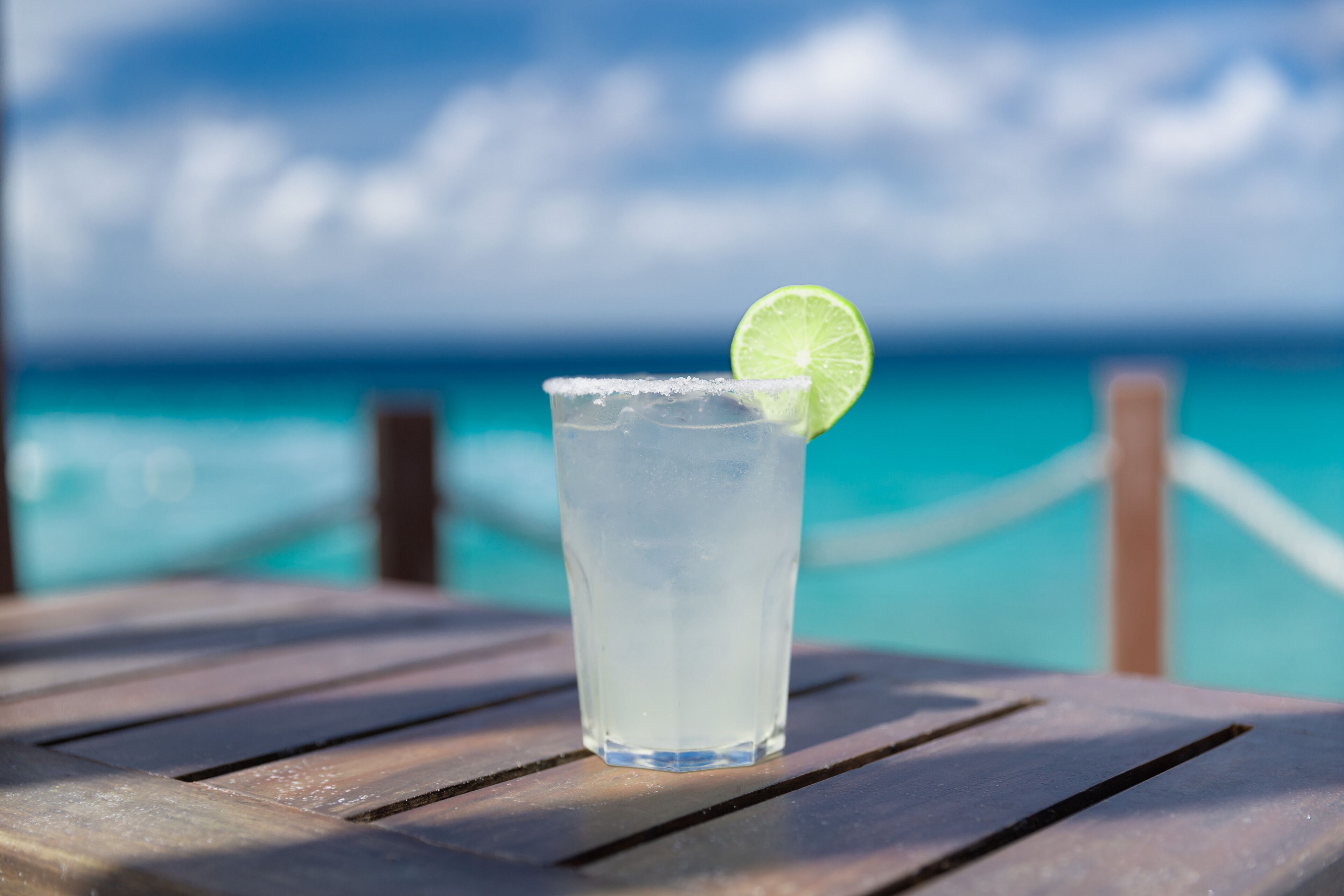 A clear glass with a lime slice on a wooden table by a poolside.