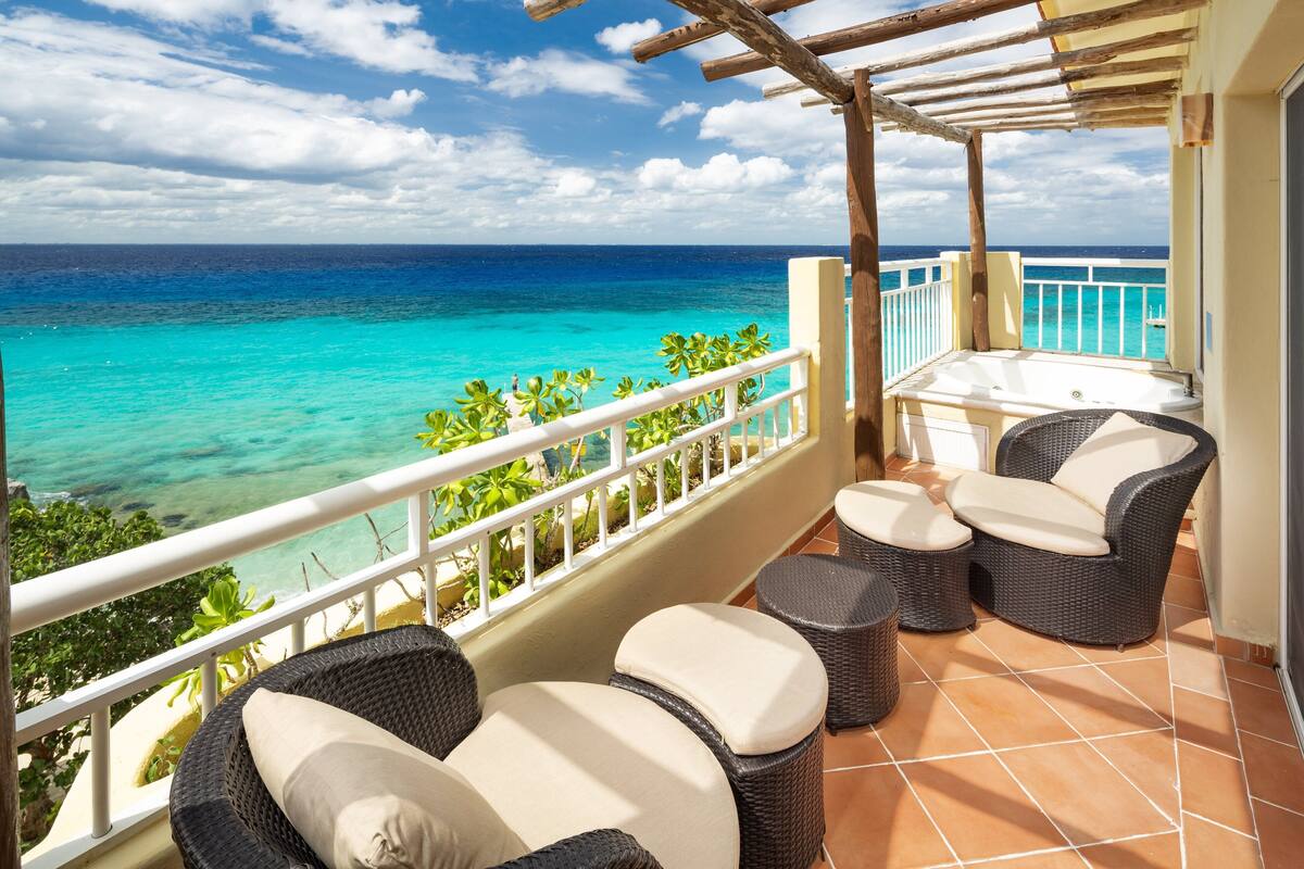 A balcony with wicker furniture, a view of the ocean, and a white railing.