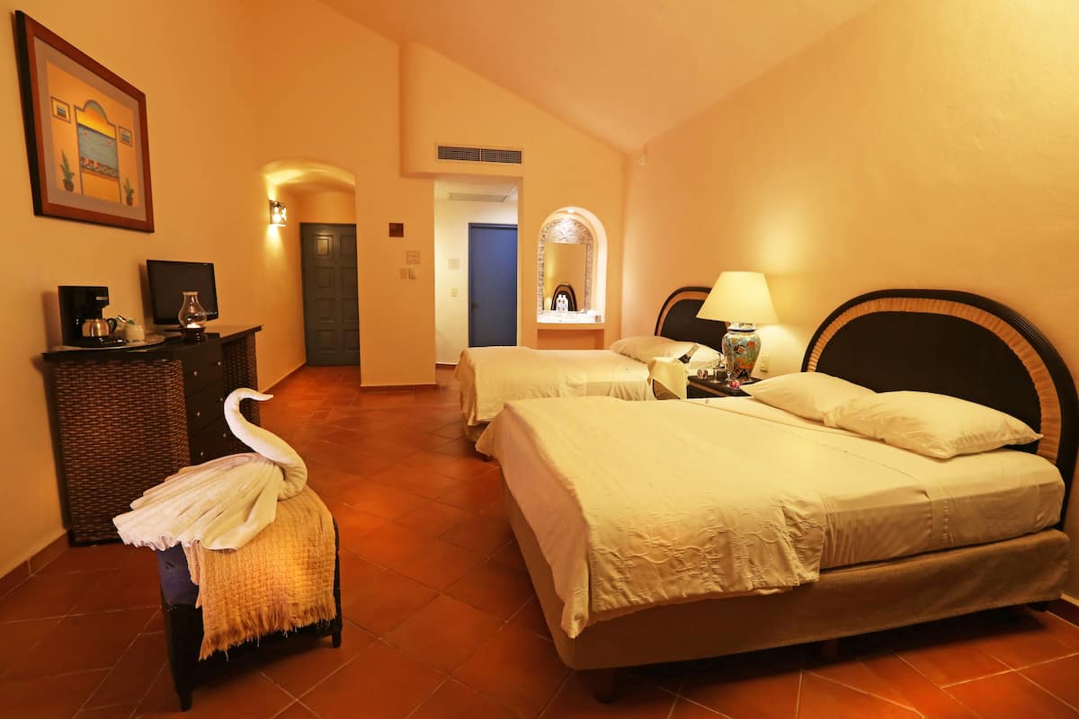 A hotel room with two beds, a desk with a computer, a chair, a lamp, and a decorative swan.