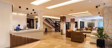 A spacious lobby with a reception desk, a staircase, and a seating area with sofas and a coffee table.