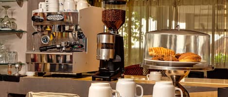 A coffee station with a coffee machine, a grinder, and a display of pastries.